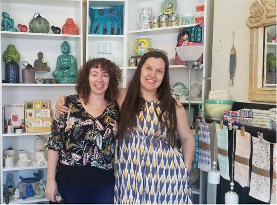 Jane and Anita pose in front of a shelf full of home decor