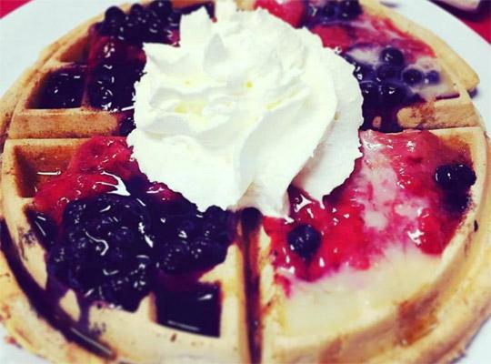 a waffle with various kinds of berry toppings and whipped cream on top