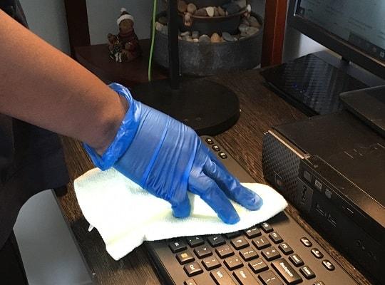 A blue gloved hand cleaning a keyboard with a white cloth