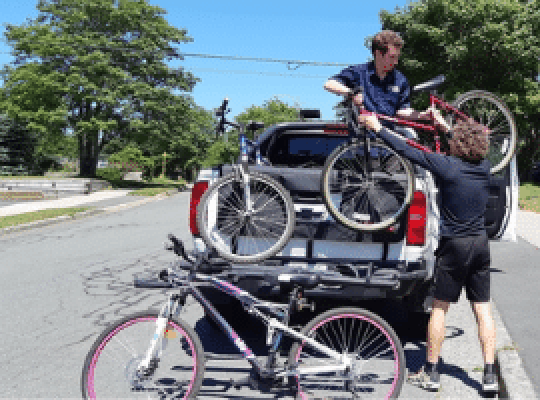 FlatOut staff lifting a bicycle into a truck on a sunny day