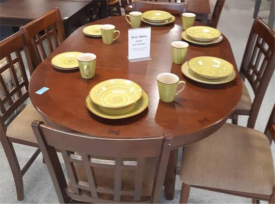 A brown wood table, chairs, and a yellow dish set laid out on top of the surface of the table.