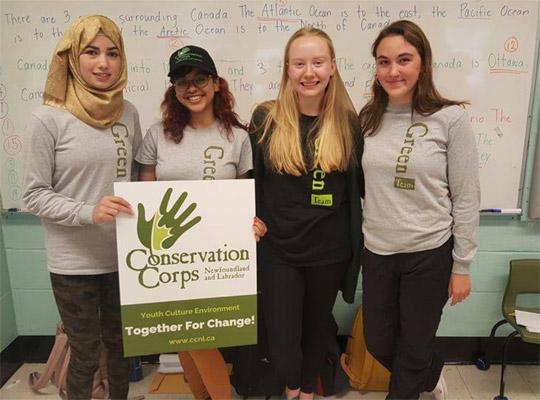 four young women holding a conservation corps sign and wearing Green Team sweaters