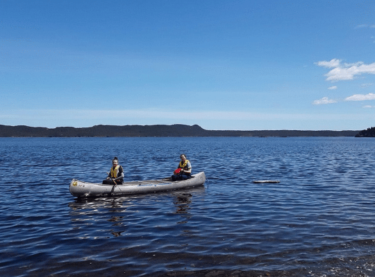 Two women paddle a canoe thought blue water under a blue sky