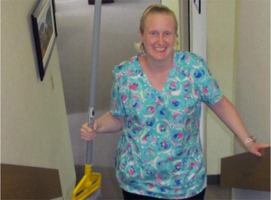 a woman wearing scrubs smiles holding a broom