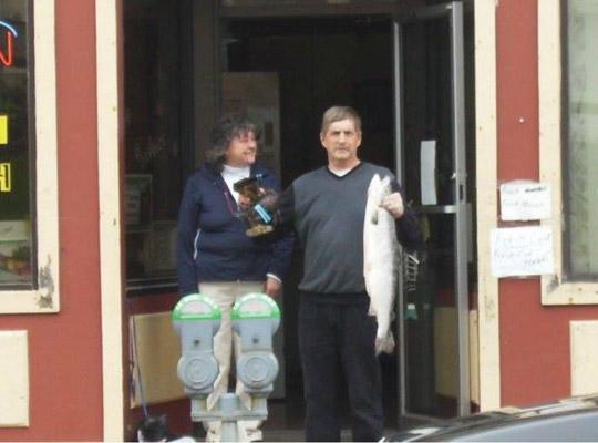 a man and a woman standing in the doorway to The Fish Depot store holding a big fish