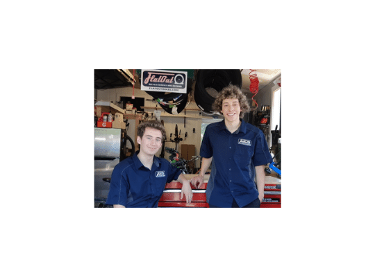 Two young men in blue shirts under the FlatOut sign in the service garage