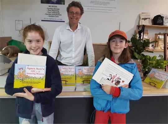 Gavin Will stands behind a book display. Two girls stand in front holding new books.