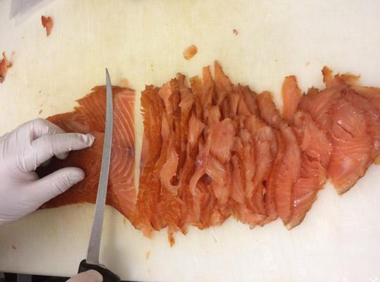 a gloved hand slicing smoked salmon with a knife