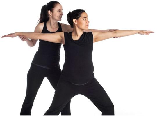 a yoga teacher guiding a pregnant woman through a yoga pose