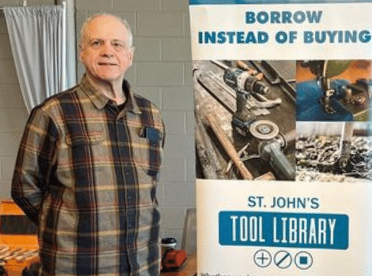 tool library manager Mike Schultz standing next to tool library banner that reads Borrow Instead Of Buying