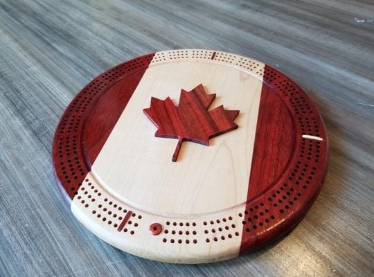 round wooden crib board designed with the colours of the Canadian flag and a maple leaf carving in the middle