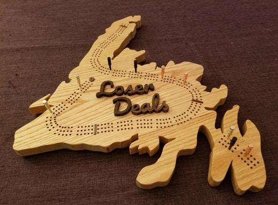 light wooden crib board in designed in the shape of Newfoundland and Loser Deals written in the middle