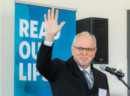 man at a microphone waving in front of a read our lips poster at the launching event