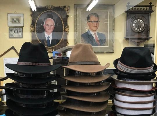 hats stacked on top of shelf and two portraits and old clocks hanging in the background