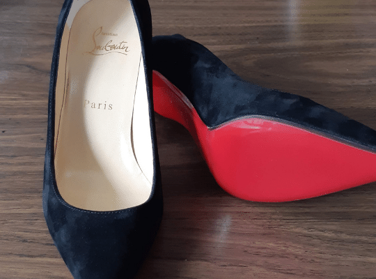 a pair of black suede Christian Louboutin shoes rest on the counter at Modern Shoe Hospital with a fresh restoration of their signature red soles