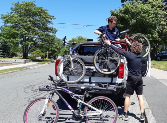 FlatOut staff lifting a bicycle into a truck on a sunny day