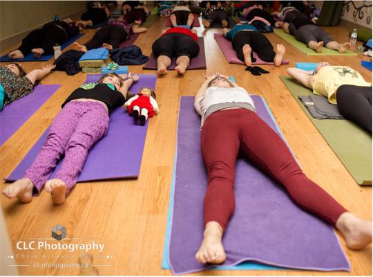 children and adults in bright colours lying down practicing yoga at Yoga Kula Co-op