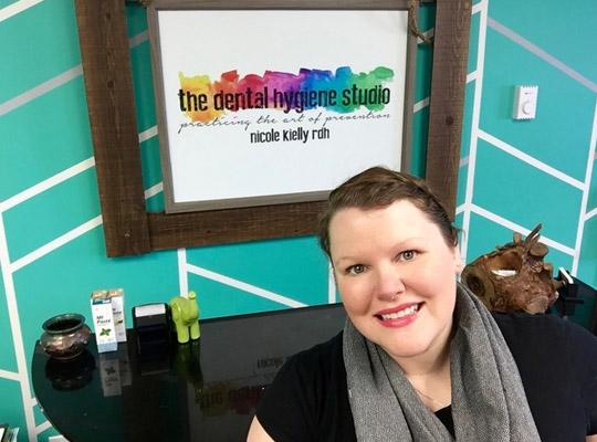 a woman smiling in front of a poster for the dental hygiene studio