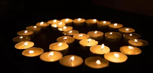 Tea light candles that are lite and are arranged in a peace symbol on a black background
