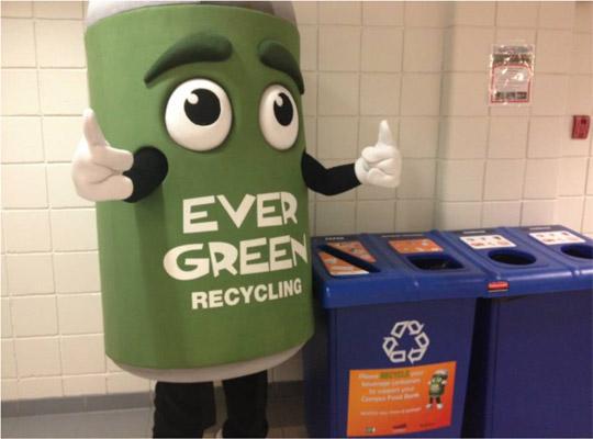 the Ever Green can mascot stands next to a recycling bin giving the thumbs up