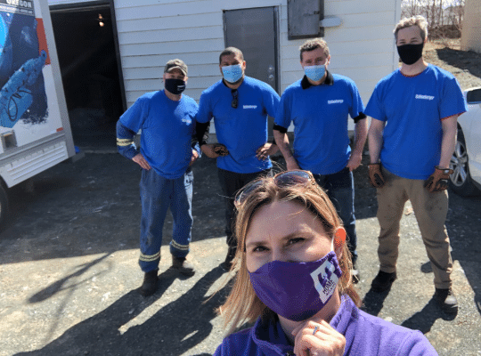 Four Home Again volunteers in blue shirts and posing for a photograph with a woman in a purple mask in the front