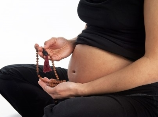 a pregnant woman holding beads by her belly