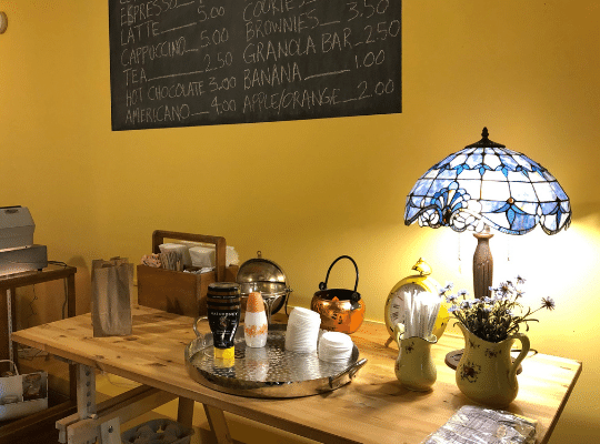Customers at Elaine's Cafe dress their coffee in a beautiful, softly lit coffee station.  The chalkboard menu is in the background on a yellow wall.