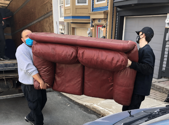 Two Home Again volunteers moving a big red leather couch