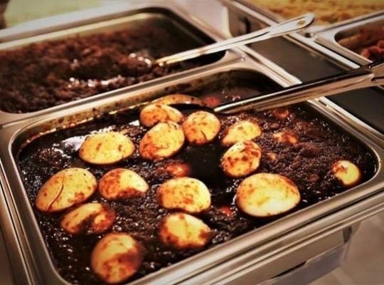 delicious looking Ethiopian food - whole potatoes with rich brown sauce - in a chafing dish with a serving spoon