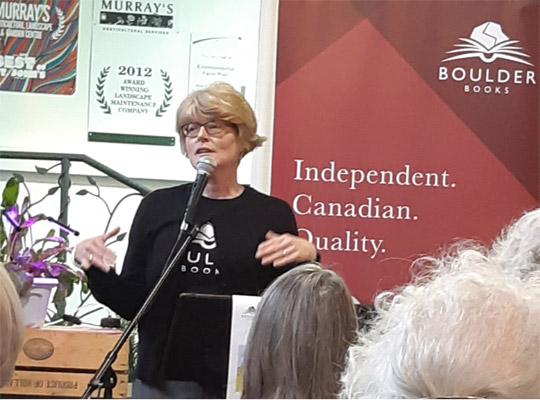 a woman gives a talk in front of a boulder books banner 